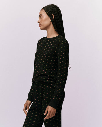 A person with braided hair is wearing The Waffle Surplus Crew in Black Mini Heirloom Rose by THE GREAT. HOL 24 ROSEBUD CAPSULE, standing against a plain background and effortlessly exuding elegance.