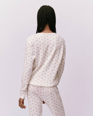 A person stands with their back to the camera, showcasing The Waffle Surplus Crew in White Mini Heirloom Rose from THE GREAT. HOL 24 ROSEBUD CAPSULE collection. Their braided hair complements the effortless style of this versatile ensemble.