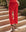 Person wearing The Reef Pant in Hot Red by THE GREAT. SP25 SWIM, featuring a comfortable fit, paired with black strappy sandals while standing on stone steps surrounded by greenery.
