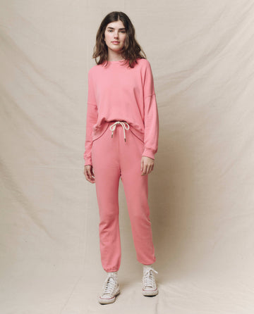 A person is standing against a neutral backdrop, wearing The Teammate Sweatshirt in Solid -- Confetti from THE GREAT. SP25 KNITS with matching sweatpants and white sneakers.