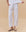 A person wears THE GREAT. PF25 HEAVY JERSEY KNITS The Jersey Win Pant in True White, paired with a white top and sandals, standing against a beige background—an effortlessly chic loungewear look.