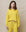 Someone wearing a daffodil-colored The Teammate Sweatshirt by THE GREAT. SP25 KNITS with matching pants stands against a plain beige background.