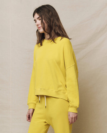 A person in The Teammate Sweatshirt, Solid -- Daffodil by THE GREAT. SP25 KNITS and matching pants exudes effortless style against a beige background, capturing the essence of casual apparel.