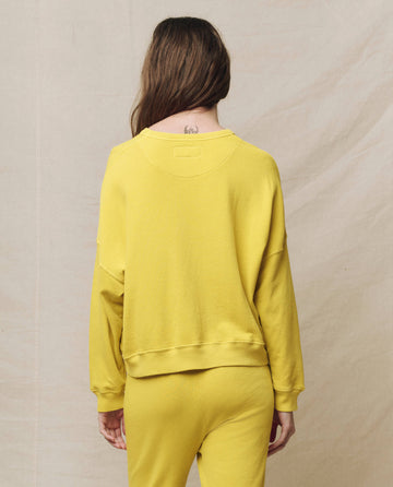 A person with long hair is wearing THE GREAT. SP25 KNITS' The Teammate Sweatshirt in Solid Daffodil, paired with matching yellow pants, against a neutral backdrop.