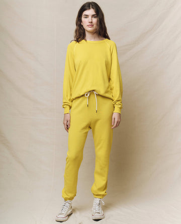 A person wearing "The College Sweatshirt" in Daffodil from THE GREAT. SP25 KNITS, paired with matching sweatpants, stands against a plain backdrop, showcasing casual collegiate style.