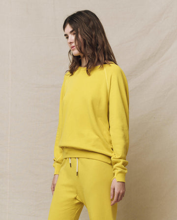 Clad in a The College Sweatshirt. Solid -- Daffodil by THE GREAT. SP25 KNITS, a person with long hair stands against a neutral backdrop, gazing thoughtfully to the side while wearing matching pants.
