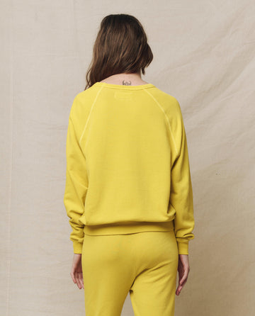 Someone in The College Sweatshirt, Solid -- Daffodil by THE GREAT. SP25 KNITS and matching pants, is facing away against a beige background.