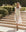 A woman wearing THE GREAT. SP25 SWIM's The Ruffle Coverup in white with ruffle shoulders walks down sunlit stone steps, embracing effortless fashion.
