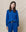 A person in college apparel, featuring The College Sweatshirt in Bright Cobalt by THE GREAT. SP25 KNITS, stands against a beige background.