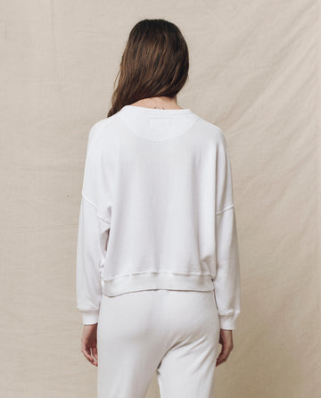 Back view of a person wearing The Teammate Sweatshirt in True White from THE GREAT. HOL 24 KNITS with white pants, standing against a plain beige background.