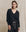 A person stands against a beige fabric background, wearing The V-Neck Sweatshirt in Almost Black by THE GREAT. FALL 24 KNITS, paired with matching black pants featuring a beige drawstring.