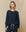 A person with shoulder-length blonde hair is wearing The College Sweatshirt in True Navy from THE GREAT. FALL 23 KNITS, along with matching pants, standing against a beige background.