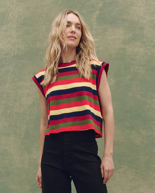 A person with long blonde hair wears THE GREAT. SU25 The Square Tee in Novelty -- Playa Stripe and black pants, standing against a plain green background.