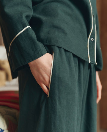 A person in THE GREAT. H25 SLEEP's Flannel Western Easy Sleep Pant in Pine & Cream, featuring classic western sleepwear style, stands with one hand in their pocket.