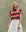 A woman stands against a green backdrop in THE GREAT. SU25 The Boxy Crew. Novelty -- Playa Stripe, paired with a red bandana and white skirt, smiling with her eyes closed.