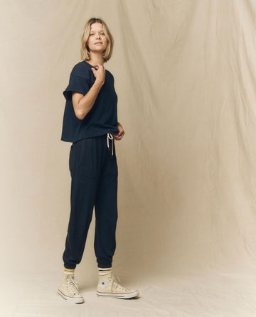 A person stands against a plain background, wearing "The Crop Tee" in True Navy from THE GREAT.'s FALL 23 KNITS collection, paired with matching sweatpants and white high-top sneakers.
