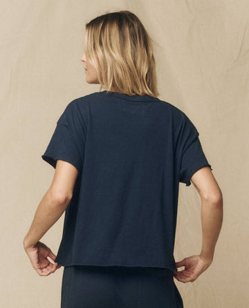A person with shoulder-length blonde hair is shown from the back, wearing The Crop Tee in True Navy by THE GREAT. FALL 23 KNITS, made of super soft cotton.