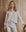 A woman wearing THE GREAT. H25 SLEEP The Crop Sleep Henley in Heather Grey and matching drawstring pants stands in front of a wooden wall.