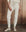 A person stands indoors in THE GREAT. H25 SLEEP The Long John. -- Washed White, paired with a matching top and gray speckled socks, against a wooden wall.