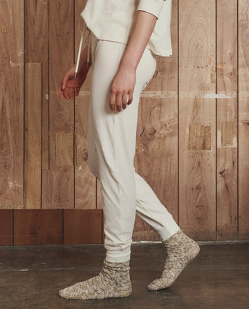 A person stands sideways in front of a wooden wall, wearing THE GREAT. H25 SLEEP's The Long John in Washed White and gray knit socks.