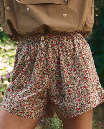 Close-up of a person wearing THE GREAT. SP26 TGO The Rover Short in Sprouting Floral and a tan shirt with a pocket, standing outdoors with greenery in the background.