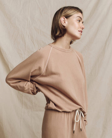 A person with short hair is wearing The College Sweatshirt, Solid - Biscotti by THE GREAT. HOL 24 KNITS, along with matching pants, standing against a neutral fabric backdrop.