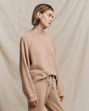 A person wearing The Slouch Sweatshirt in Solid Biscotti from THE GREAT. HOL 24 KNITS, along with matching pants, stands effortlessly against a textured beige background.