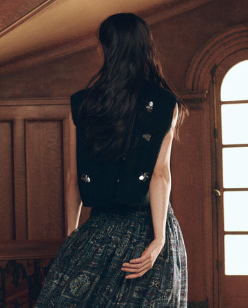 The Embellished Sweater Vest in black with silver floral details, worn over a patterned skirt.