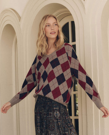 A person wearing The Argyle V-Neck Pullover in Heather Grey, a grey argyle V-neck pullover with a red and navy blue pattern.