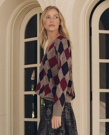 A person wearing a The Argyle V-Neck Pullover in Heather Grey, a grey argyle V-neck pullover with a red and navy blue pattern.
