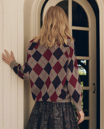 Person from behind wearing a Heather Grey The Argyle V-Neck Pullover with a maroon and navy pattern, paired with a patterned skirt.