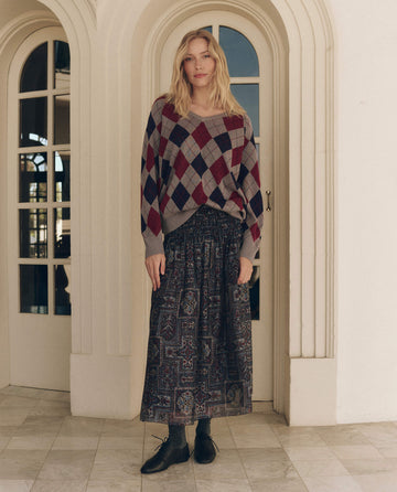 A person wearing a Heather Grey The Argyle V-Neck Pullover and a long, patterned maxi skirt.