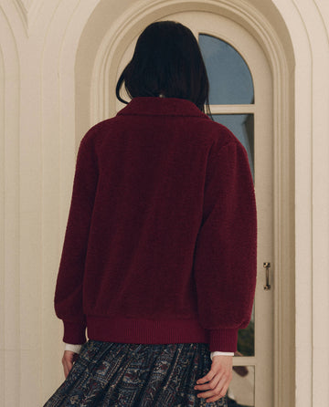 Back view of a person wearing The Patch Pocket Plush Jacket in maroon, featuring a textured design, a collar, patch pockets, and ribbed cuffs.