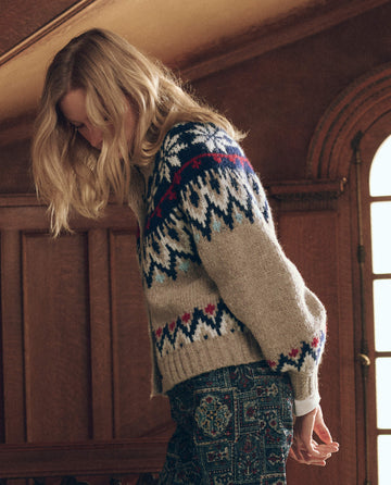 A person wearing The Winter Fairisle Cardigan. -- Snowflake, a beige, button-down winter cardigan with a colorful snowflake pattern across the yoke and cuffs.