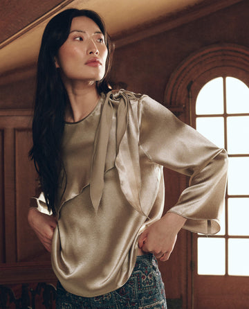 A model wearing The Scarf Tie Top. -- Gold Shimmer, a long-sleeved, gold-toned metallic top with a shoulder detail.