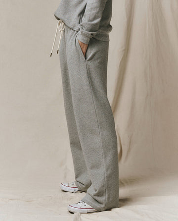 Model wears SP26 New Knits' The Horseshoe Sweatpant in Solid Varsity Grey with a matching sweatshirt, hands in pockets, standing on a beige fabric background and finished with white sneakers.