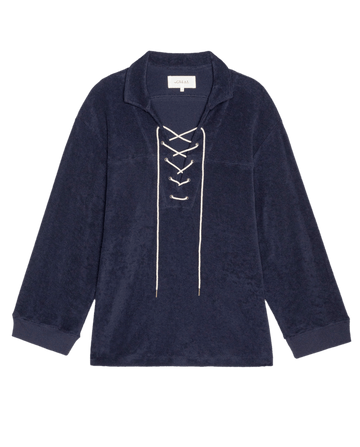 The Micro Terry Lace Up Tunic by THE GREAT. SU26 features a navy blue color, long sleeves, a collar, and white lace-up front detail in soft micro terry fabric, shown on a plain white background.