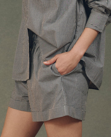 A person stands against a plain background, wearing THE GREAT. SP25 D2's The Boxer Short in Black And White Gingham with one hand casually in the pocket, exuding a comfortable fit akin to men's underwear.