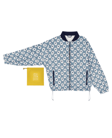 The Reversible Ultra Light Down Puffer in Falling Daisy and Cream by THE GREAT. SP25 TGO, featuring a navy collar for added comfort, is displayed with a small yellow pouch.