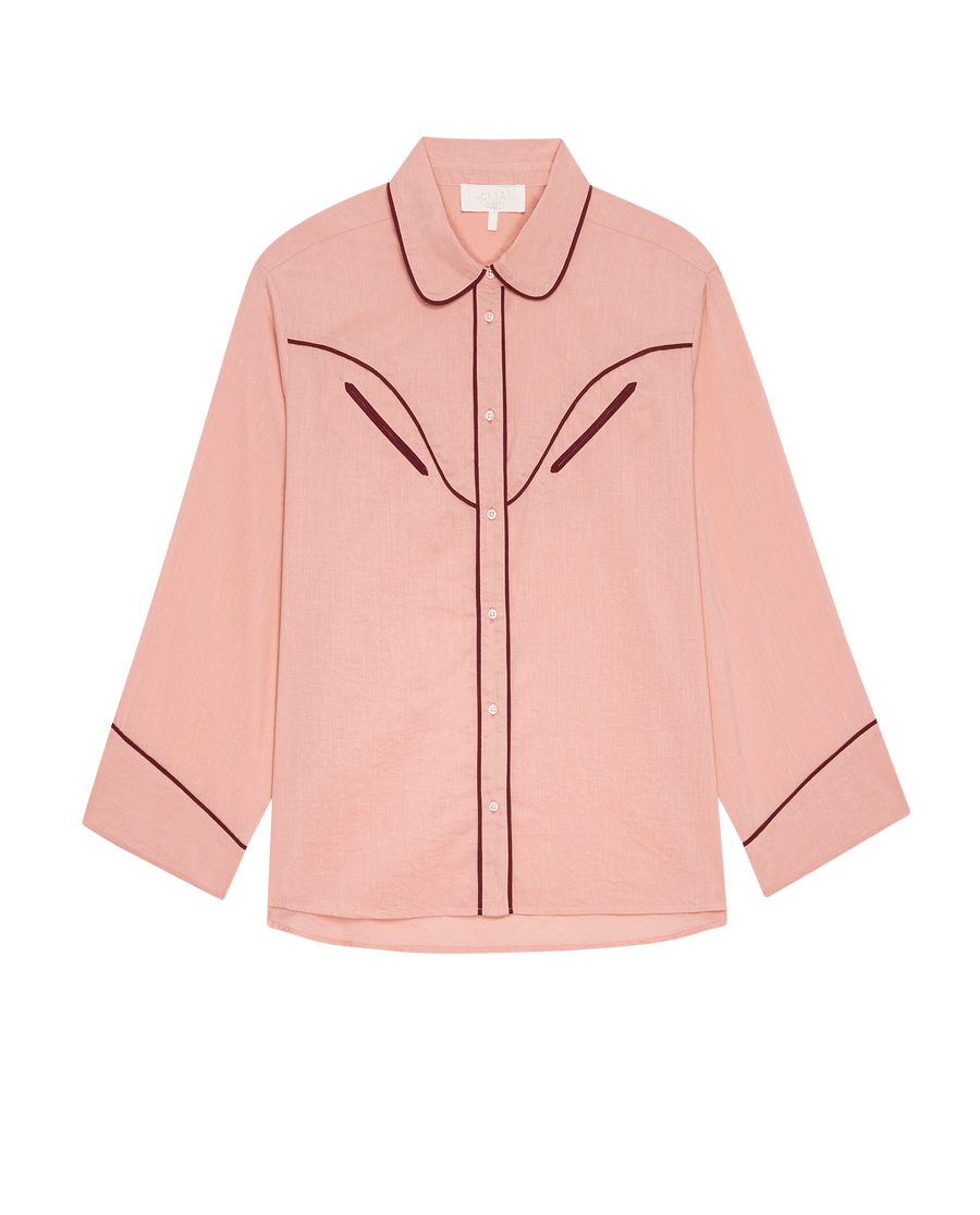 The Western Pajama Shirt -- Rose Bloom by THE GREAT. SP25 SLEEP features light pink fabric, long sleeves, and dark piping on the collar, chest, and cuffs, shown against a plain background.