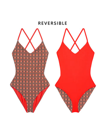 Two reversible "The Reversible Lace Up One Piece" swimsuits by THE GREAT. SP25 SWIM, shown front view: one side in rust tile print, the other hot red; both with crisscross lace-up straps. Text reads "REVERSIBLE.
