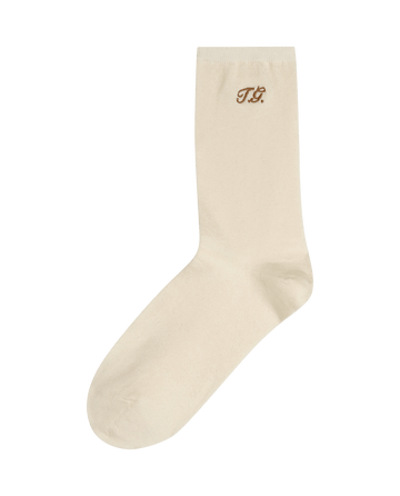 The Monogrammed Trouser Sock in cream by THE GREAT. F25 D1 ACCESSORIES features brown "T.G." initials near the top.