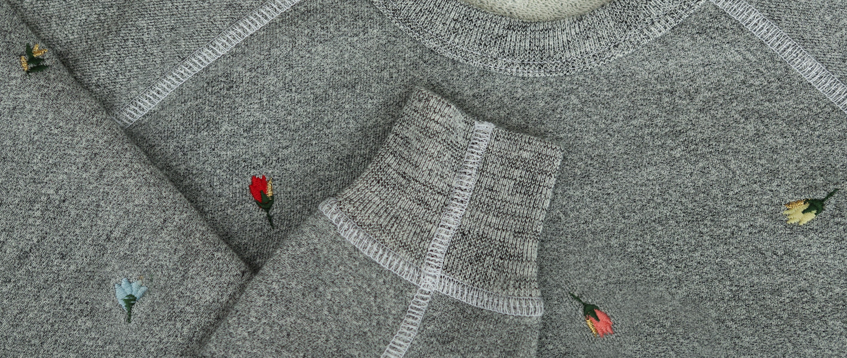 Close-up of a gray knit fabric with white seams and small embroidered flowers in red, yellow, and blue.