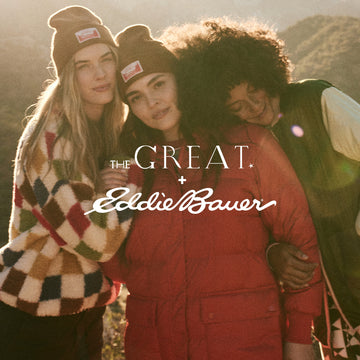 Three people wearing colorful winter clothing stand outdoors with mountains in the background.