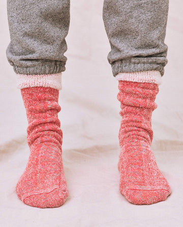 A person in a cozy gray sweatshirt with matching sweatpants and THE GREAT. SP25 SWEATSHIRT SOCKS in Red Cherry stands on a light surface.