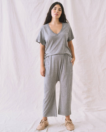 A person wearing The V-Neck Tee in Heather Grey from THE GREAT. SP22 APRILCAP, along with matching loose-fitting pants, stands in front of a plain white background.