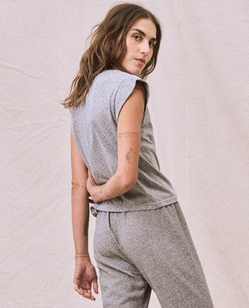 Person with long hair wearing a Heather Grey Peak Shoulder Tee by THE GREAT. FALL 22 KNITS and matching high-waisted denim, hand resting on hip, looking over their shoulder against a neutral background.